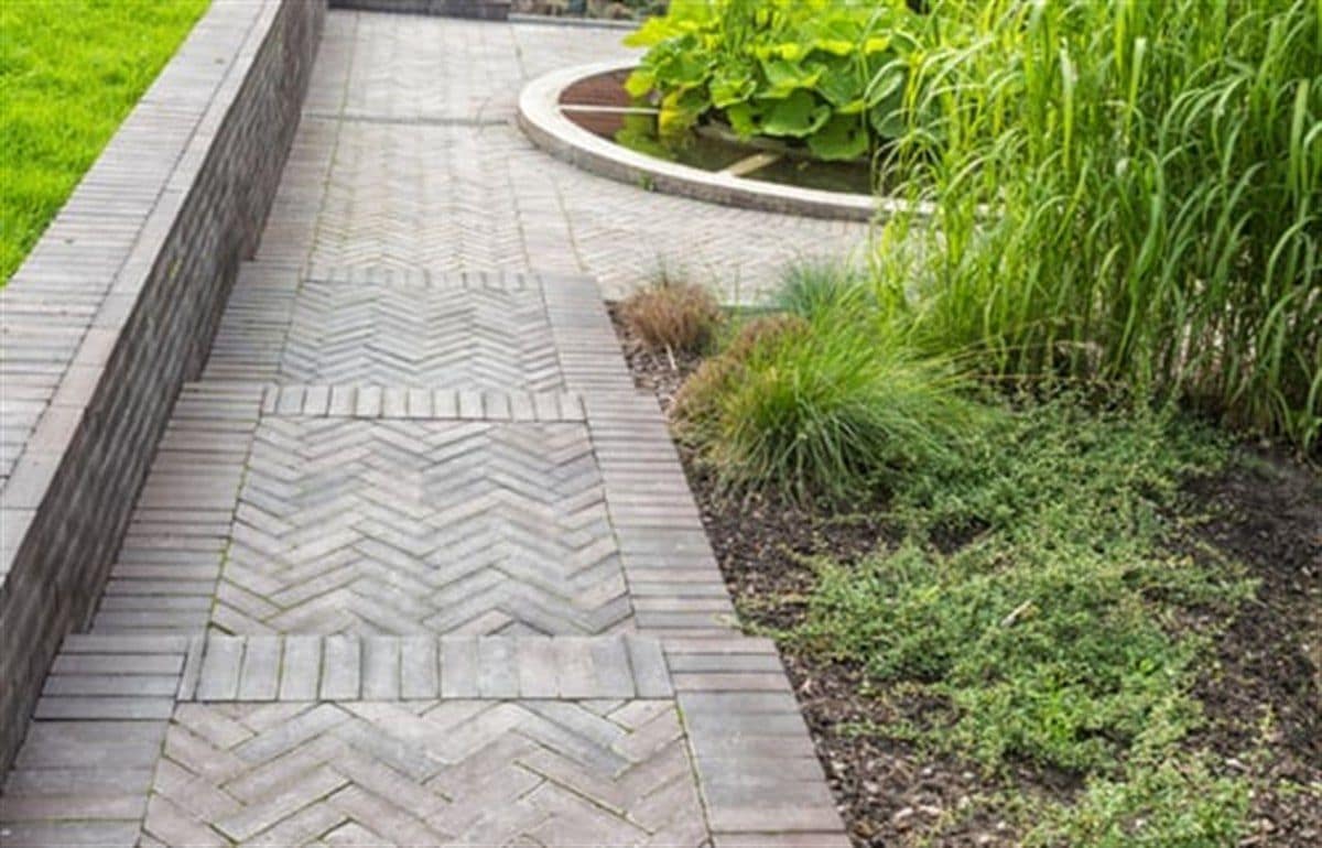 Interlocking paver walkway bordered by planted beds and trimmed hedges
